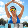 A woman wearing orange anti-fog UV swim goggles is shown against a bright blue sky and water background.