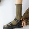A close-up of a person wearing olive green tube socks and a brown knitted cuff, paired with black sandals.