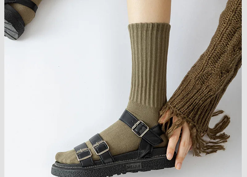 A close-up of a person wearing olive green tube socks and a brown knitted cuff, paired with black sandals.