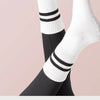 A close-up of white and black striped non-slip yoga socks worn on a foot against a light pink background.