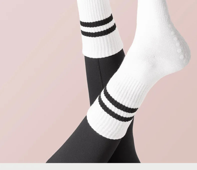 A close-up of white and black striped non-slip yoga socks worn on a foot against a light pink background.