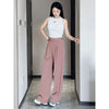 A woman models loose rose pink yoga pants and a white sleeveless top in a hallway.