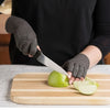 A person wearing dark gloves is slicing an apple on a wooden cutting board.