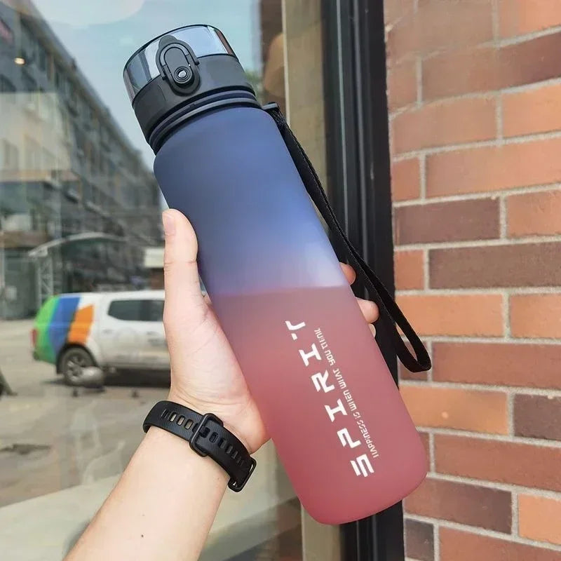 A hand holds a gradient insulated sports water bottle with pink and blue tones against a brick wall background.