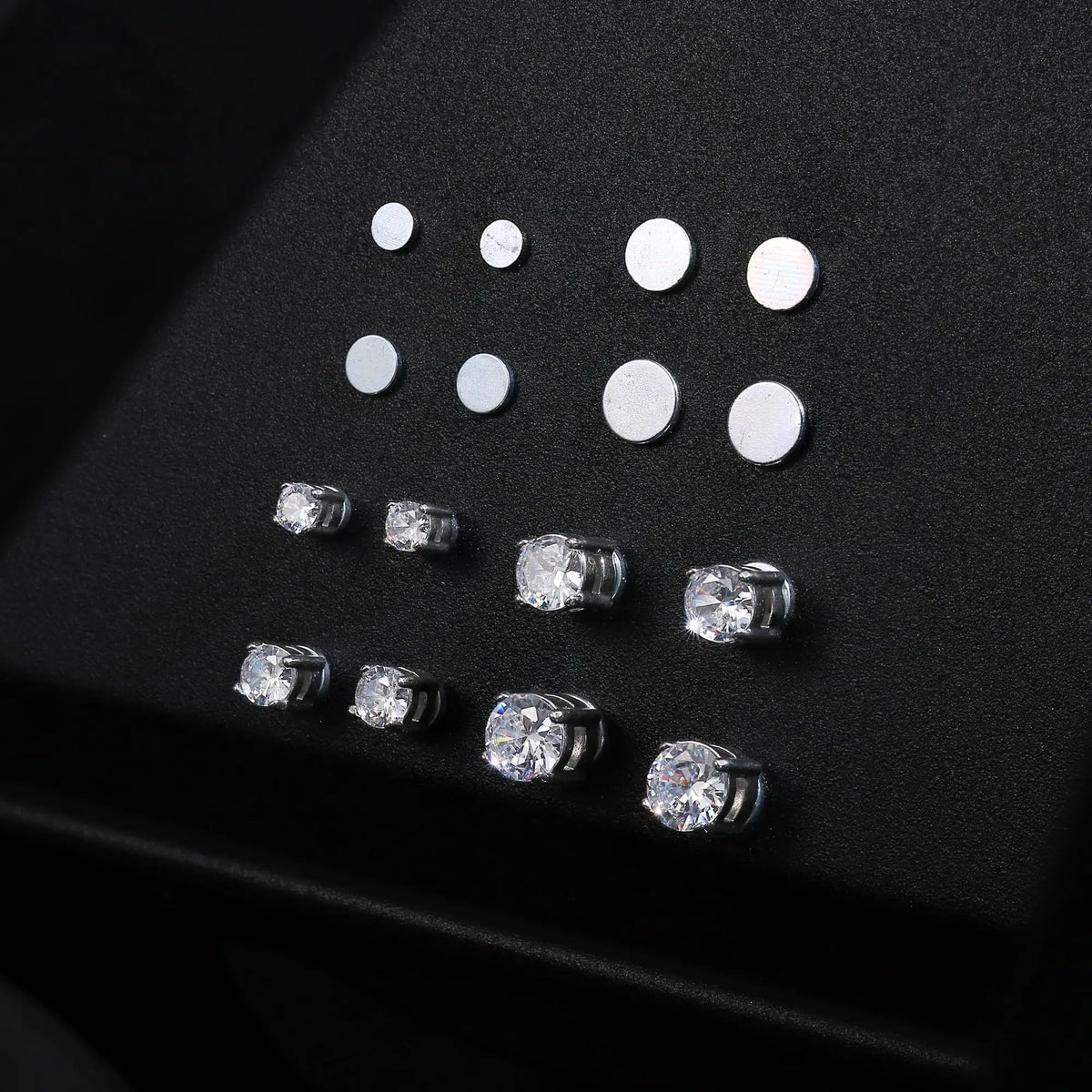 A collection of magnetic cubic zirconia stud earrings arranged on a dark surface.