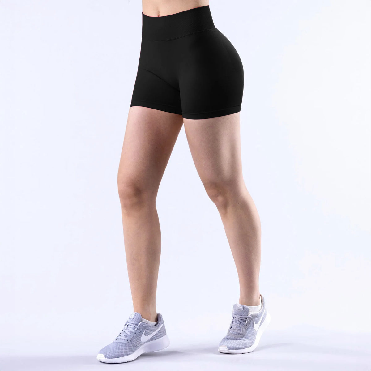 A person wearing black seamless high-waisted yoga shorts and white athletic shoes.