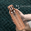 A hand holds an insulated copper water bottle with a textured anti-slip grip against a dark background.