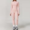 A woman wearing a light pink, long-sleeved athletic top and matching leggings with white socks and gray sneakers.
