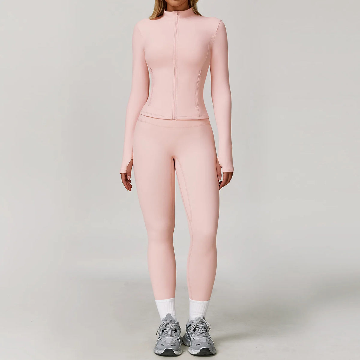 A woman wearing a light pink, long-sleeved athletic top and matching leggings with white socks and gray sneakers.