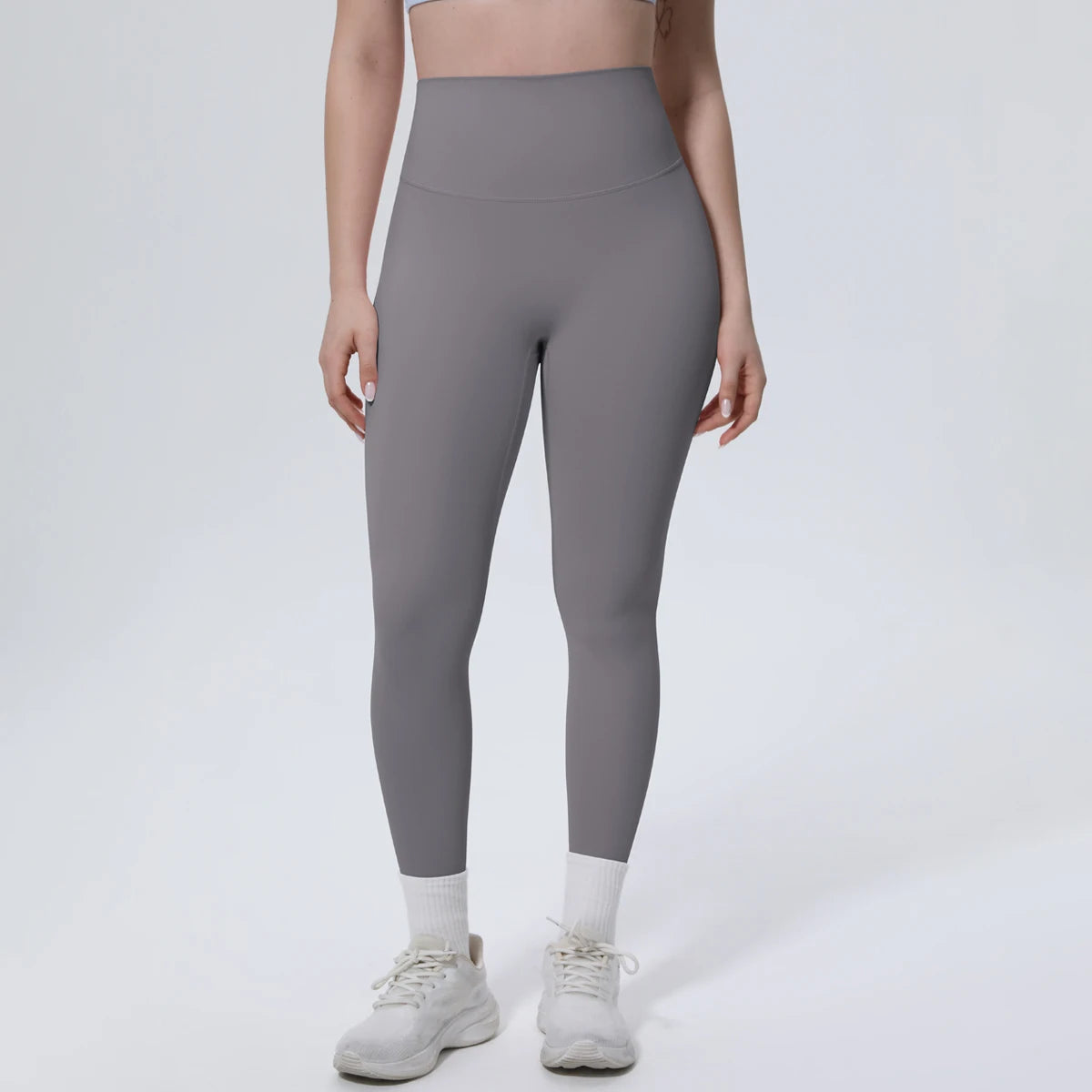 A model is wearing high-waisted gray quick-drying yoga and fitness leggings with white socks and light-colored athletic shoes