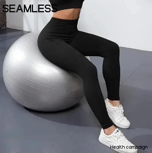 Une personne portant des leggings de yoga noirs et sans coutures est assise sur une balle d'exercice argentée.