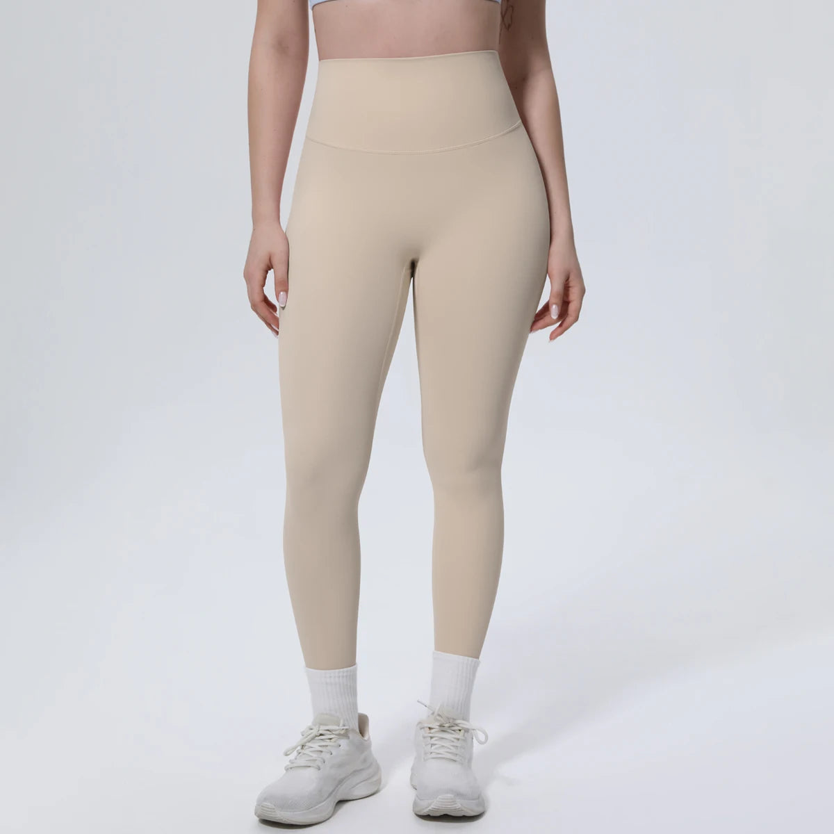 A model wearing beige high-waisted quick-drying yoga and fitness leggings with white socks and white athletic shoes.