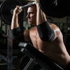 A muscular man lifts a heavy black dumbbell during a workout, wearing black compression sleeves.