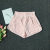 Light pink women's high-waist yoga and fitness shorts laid flat on a dark gray surface with a white card and pink roses.