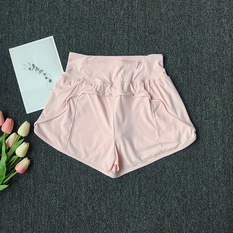 Light pink women's high-waist yoga and fitness shorts laid flat on a dark gray surface with a white card and pink roses.