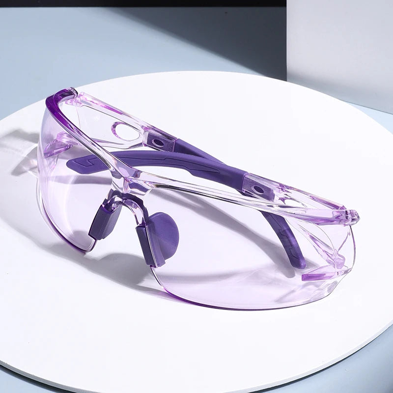A pair of purple transparent safety goggles resting on a white surface.
