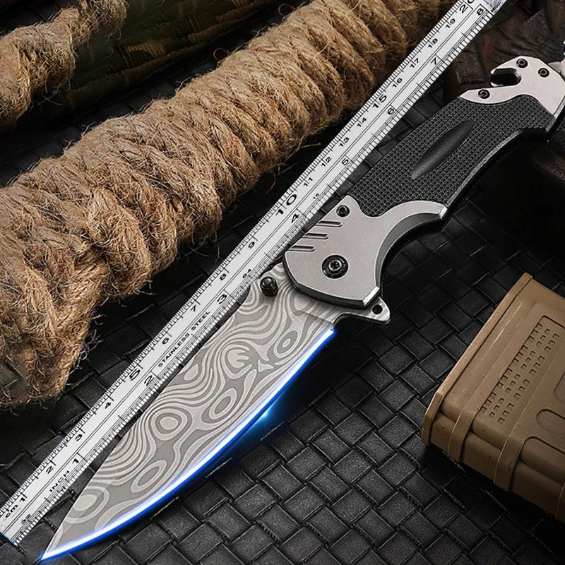 A multi-functional folding survival knife with a silver blade and black handle rests on a dark surface next to a measuring ru