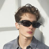 A close-up portrait of a man wearing black spiked rivet sunglasses against a bright background.