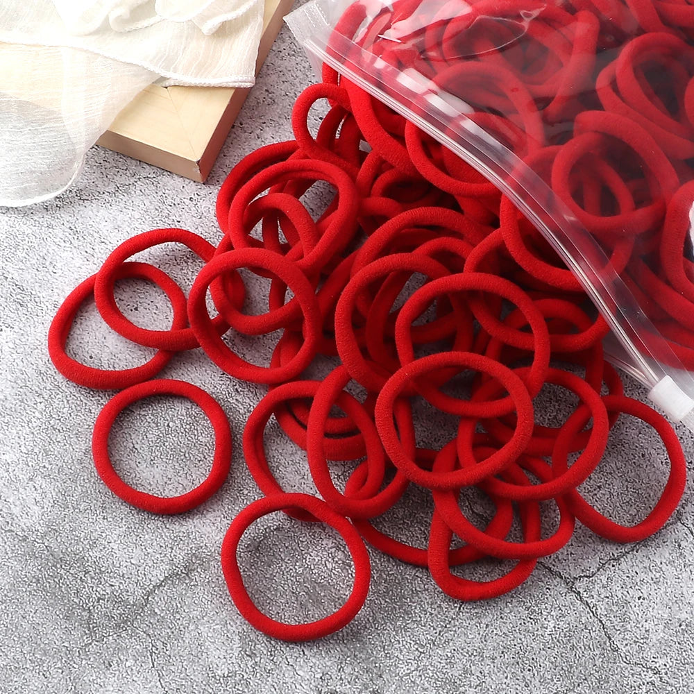 A pile of red elastic hair bands in a clear plastic bag on a gray surface.