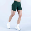 A person wearing dark green seamless high-waisted yoga shorts and white socks standing against a light background.