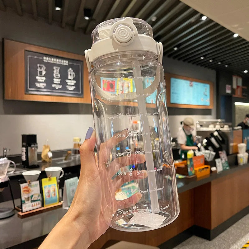 A hand holds a clear plastic water bottle with a straw and time scale markings in a cafe setting.