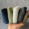 A hand holds a pack of four merino wool hiking socks in various shades of green, gray, and black.
