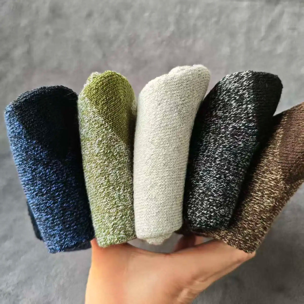 A hand holds a pack of four merino wool hiking socks in various shades of green, gray, and black.