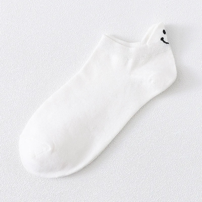 Calcetines blancos de tobillo con una carita sonriente negra bordada en la punta.