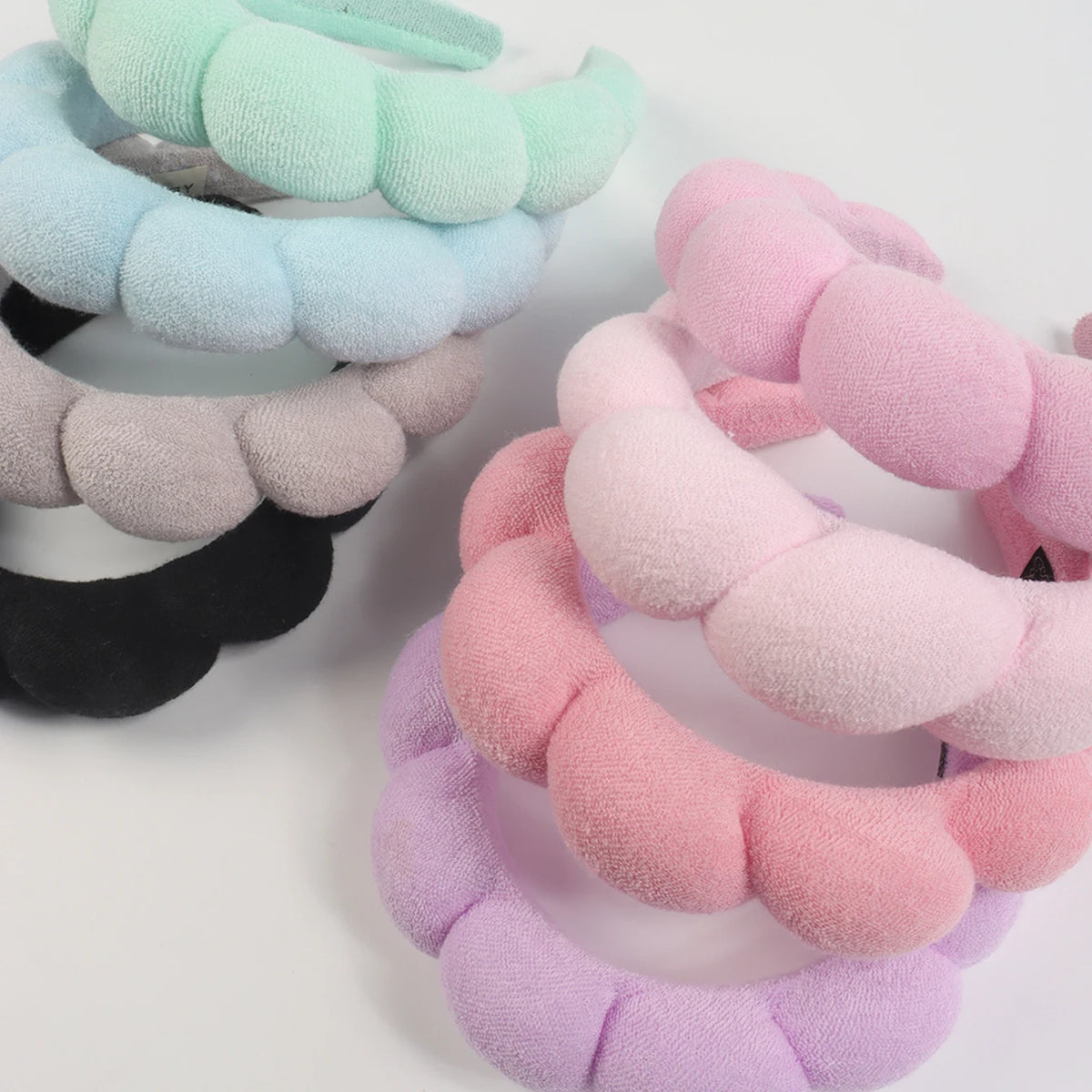 A set of stacked microfiber skincare headbands and wristbands in pastel shades of mint green, blue, gray, pink, and purple.