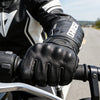 Black leather riding gloves worn by a person on a motorcycle.