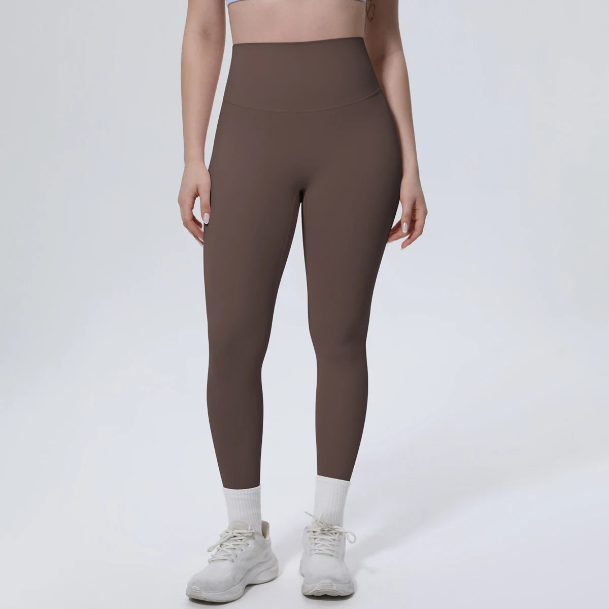 A model wearing high-waisted, dark brown quick-drying yoga leggings and white socks, standing against a light background.