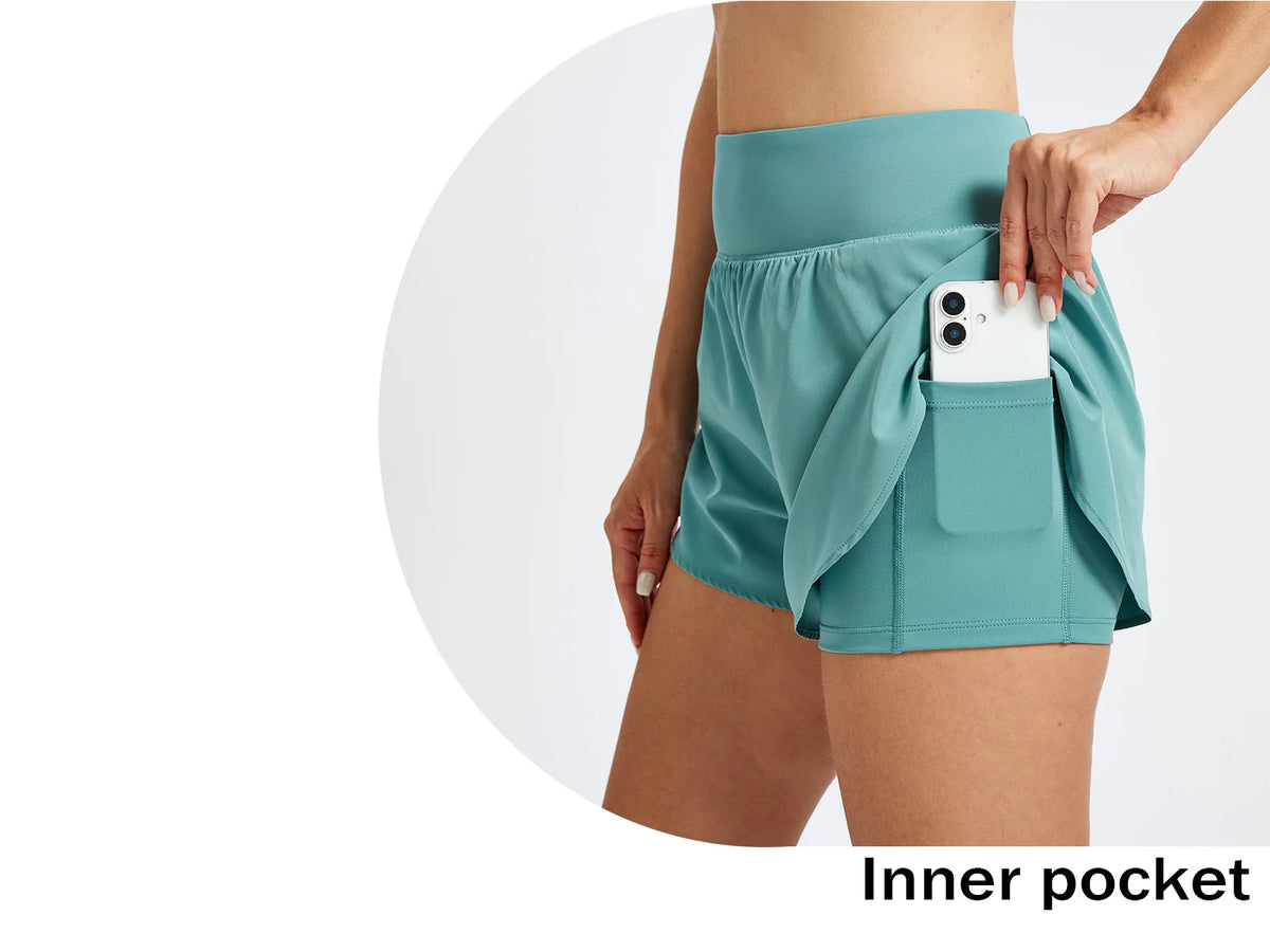 Eine Person trägt tealfarbene, hochgeschnittene Sportshorts mit einer Innentasche für ein Smartphone.