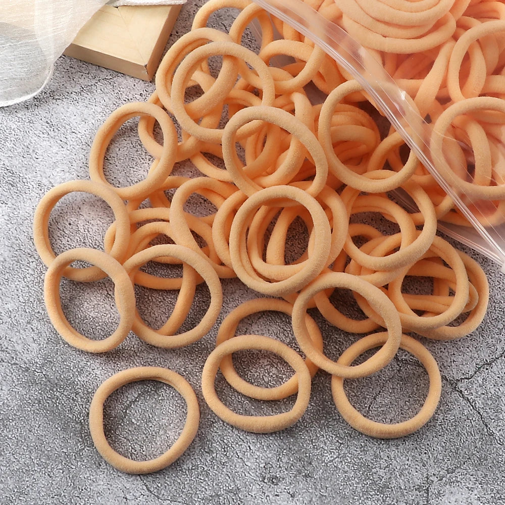 A pile of 50 elastic hair bands in various shades of orange and tan coiled on a gray surface.