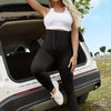 A woman models high waisted black shaping leggings and a white crop top while leaning into the open trunk of a car.