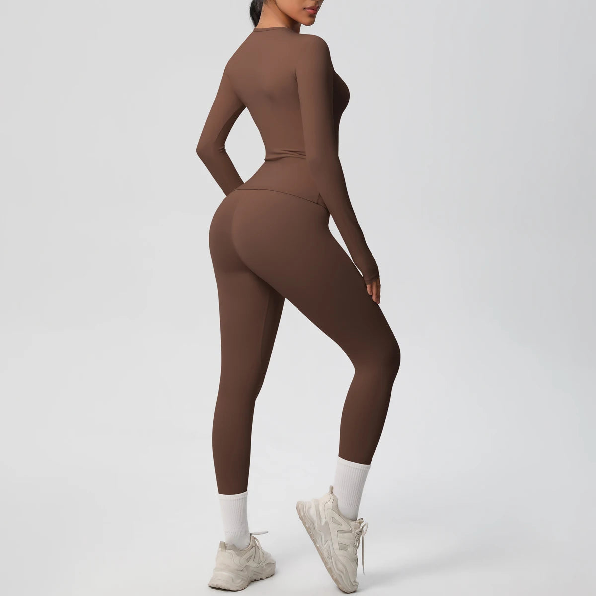 A woman wearing a full-length, long-sleeved performance yoga and gym set in a solid brown color.