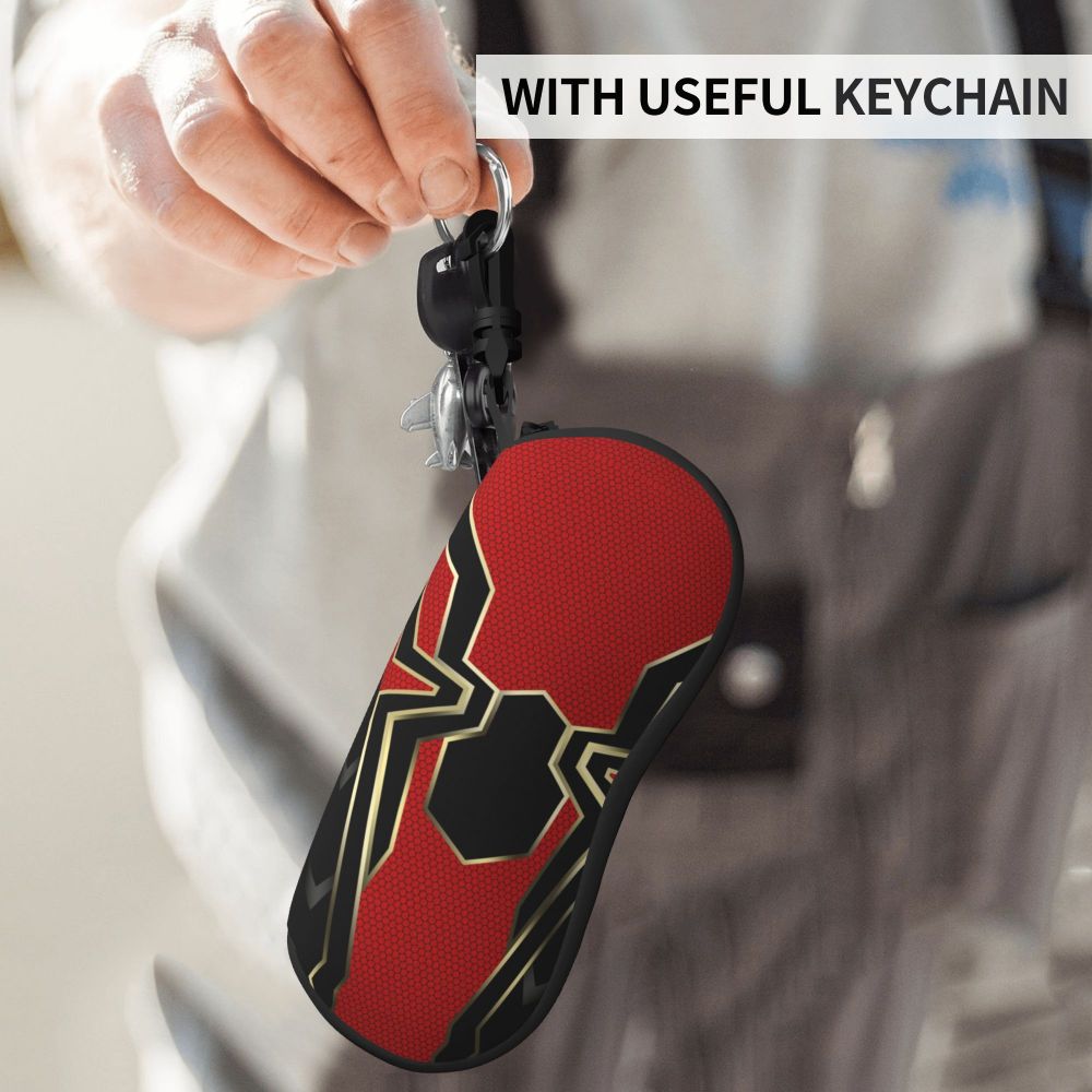 A hand is holding a black keychain featuring a red and black spider web design on the sole of an eyeglass pouch.