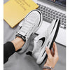 A pair of white and black casual shoes shown on a foot next to a laptop and a yellow book.