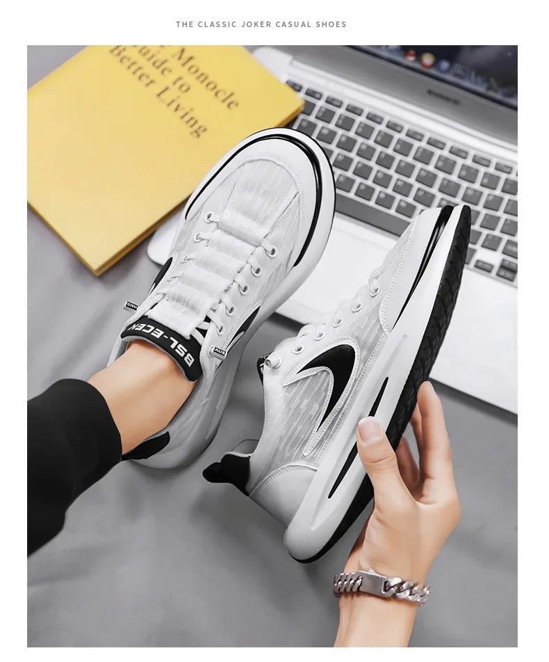 A pair of white and black casual shoes shown on a foot next to a laptop and a yellow book.