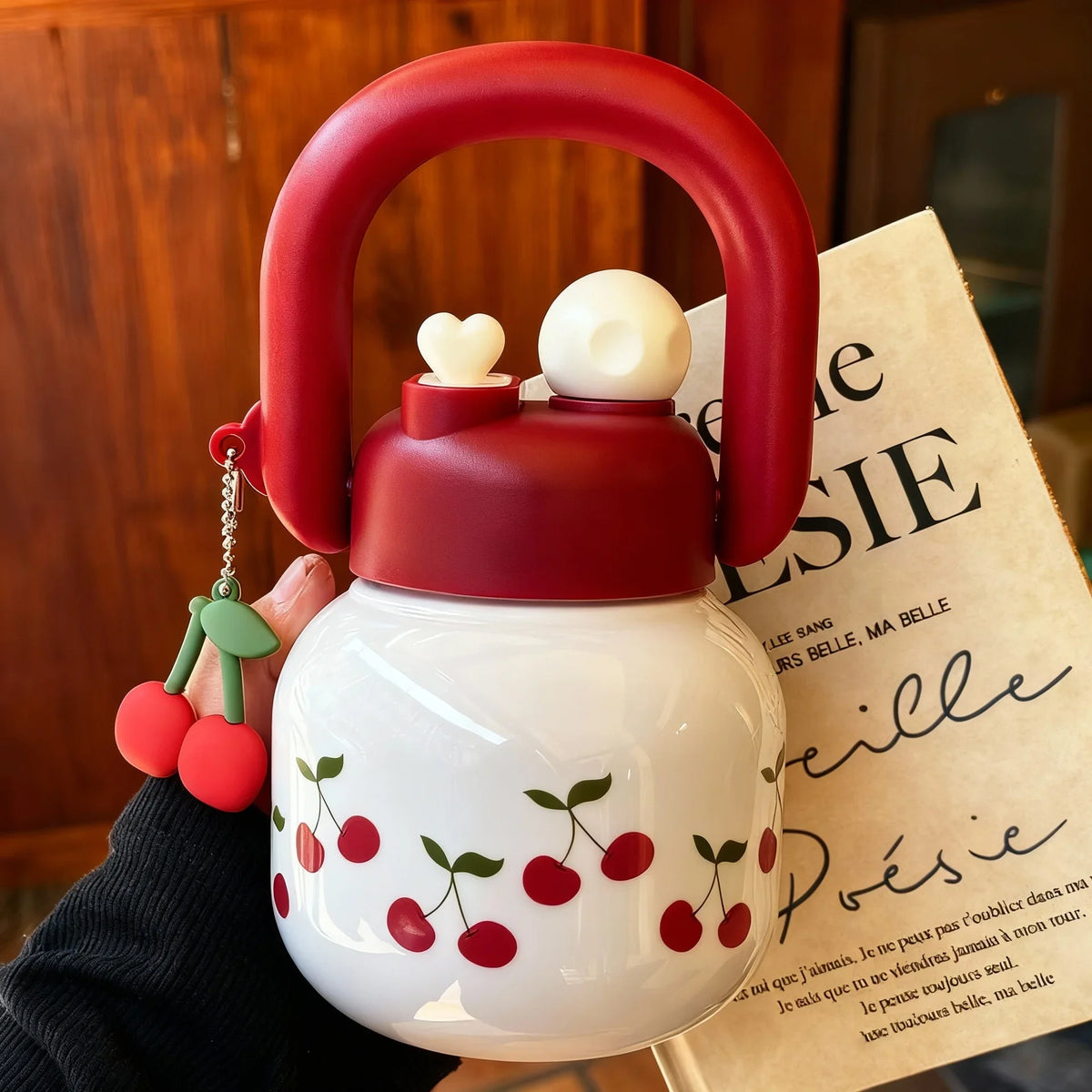 Una botella de agua aislada roja con tapa y sorbete blanca, sostenida por una mano sobre un libro.
