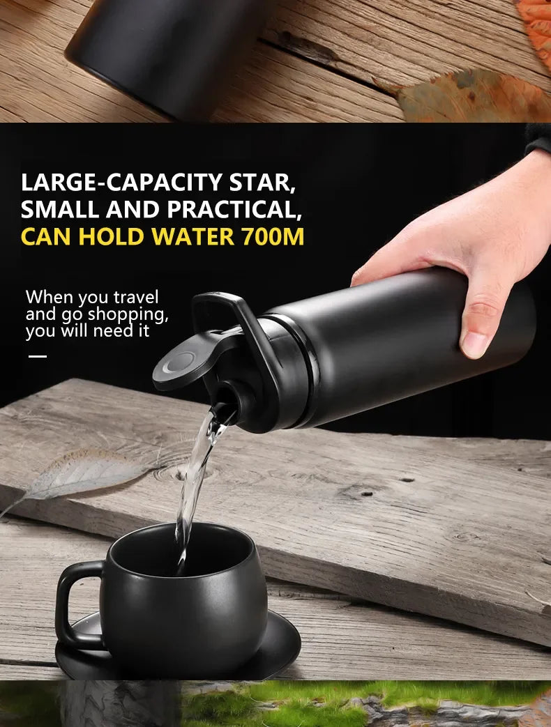 A black leakproof aluminum portable water bottle is shown pouring water into a black mug on a wooden surface.