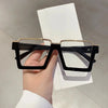 A pair of black and gold oversized square semi-rim metal eyeglasses held against a white background.