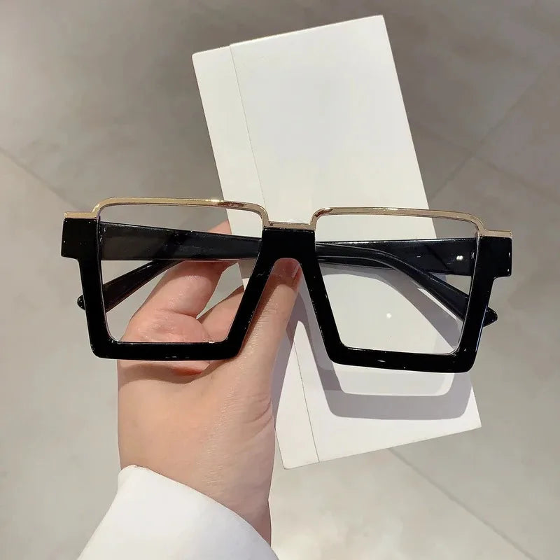 A pair of black and gold oversized square semi-rim metal eyeglasses held against a white background.
