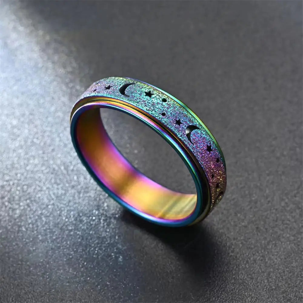 A close-up of a stainless steel spinning ring featuring a purple iridescent finish with moon and star designs.