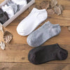 Una colección de calcetines tobilleros blancos, grises y negros exhibidos sobre una superficie de madera.