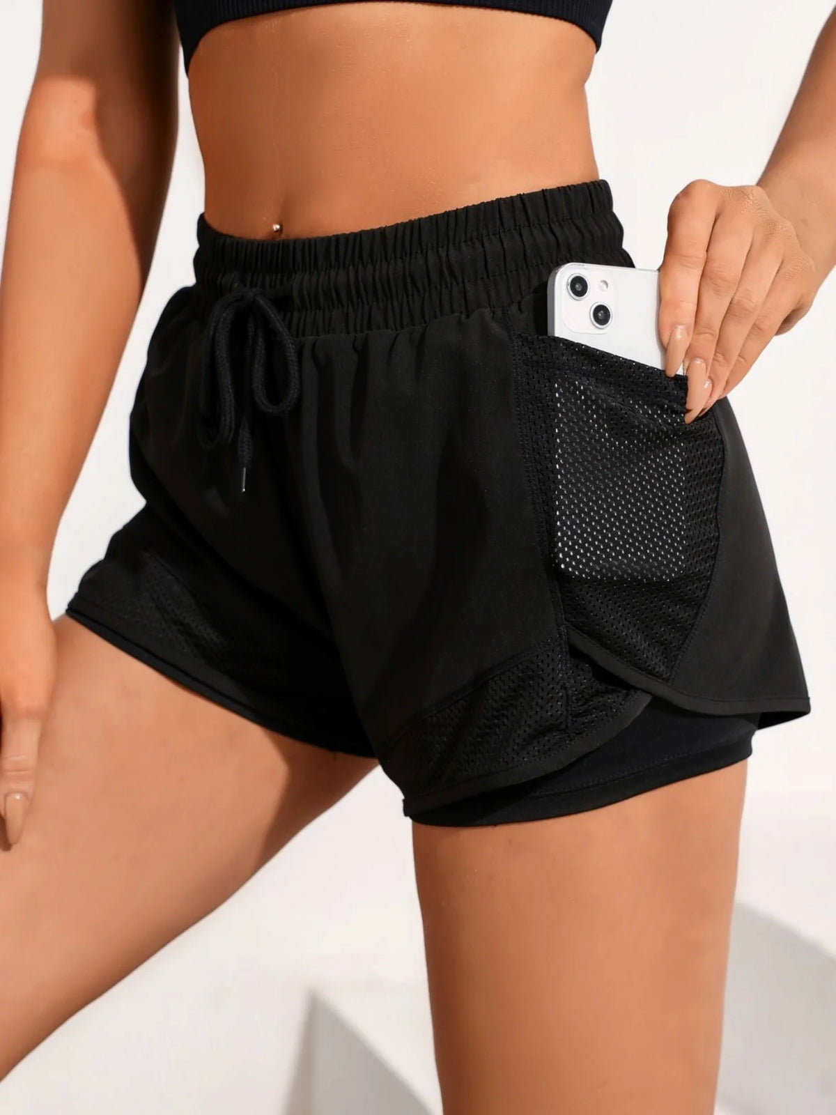 A person wearing black athletic shorts with a mesh pocket and a black sports bra top.