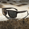 A pair of dark-framed sunglasses resting on a rough, light-colored rock against a sandy background.