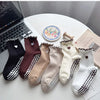 A collection of embroidered yoga socks in various colors including black, maroon, beige, and cream, displayed on a white surf