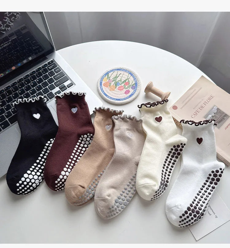 A collection of embroidered yoga socks in various colors including black, maroon, beige, and cream, displayed on a white surf