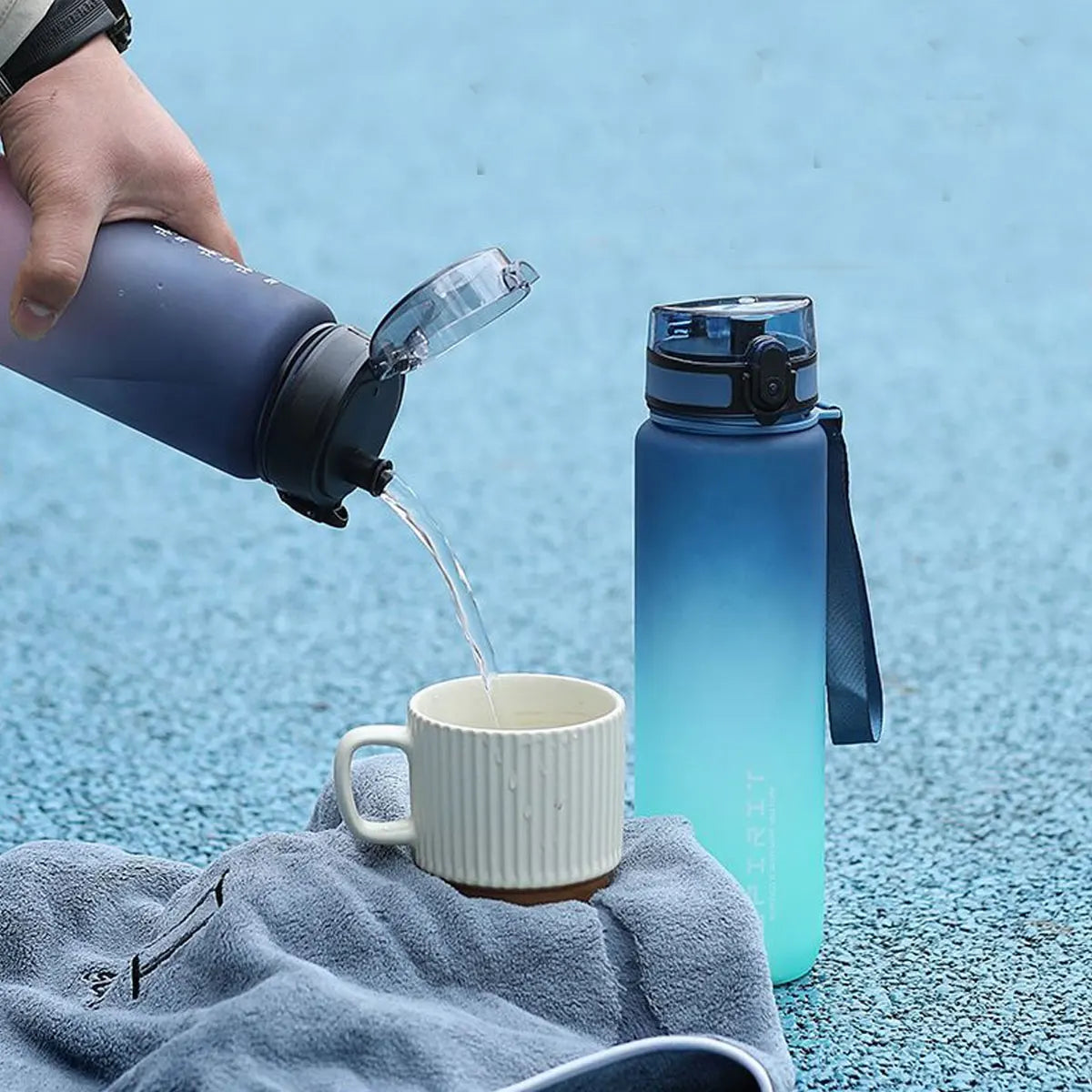 Eine Hand gießt Wasser aus einer dunklen Flasche in eine weiße Tasse vor blauem Hintergrund.