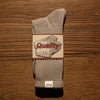 A pair of gray tube socks with a quality label featuring the word Quality on the front, resting on a wooden surface.